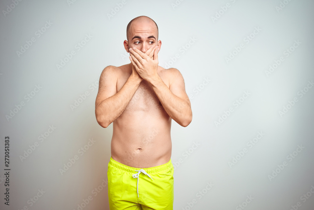 Fototapeta premium Young shirtless man on vacation wearing yellow swimwear over isolated background shocked covering mouth with hands for mistake. Secret concept.