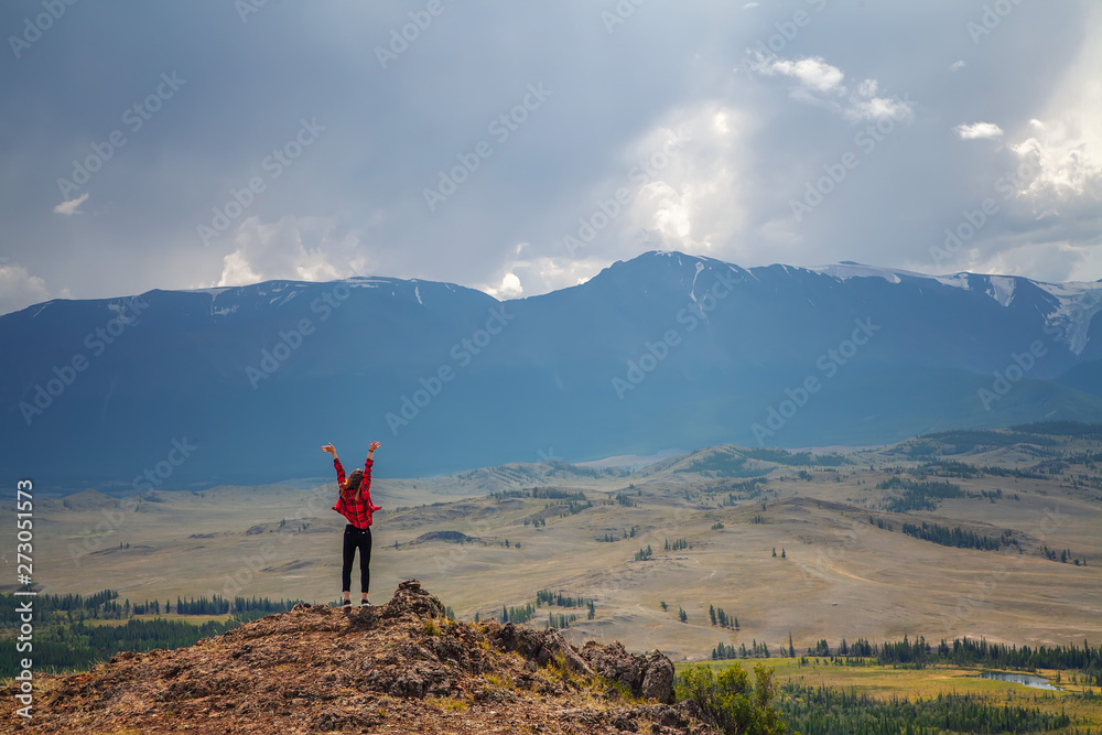 mountain landscape. teen girl in red plaid shirt rejoices, spread her arms up against the background of mountain peaks