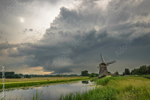 Supercell thunderstorm with rotating wallcloud over the countryside of Holland. Classic dutch scene with a canal and windmill.
