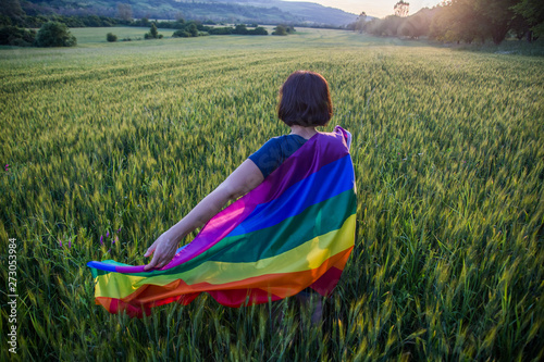 Woman holding the Gay Rainbow Flag on a green meadow outdoors. Happiness, freedom and love concept for same sex couples.