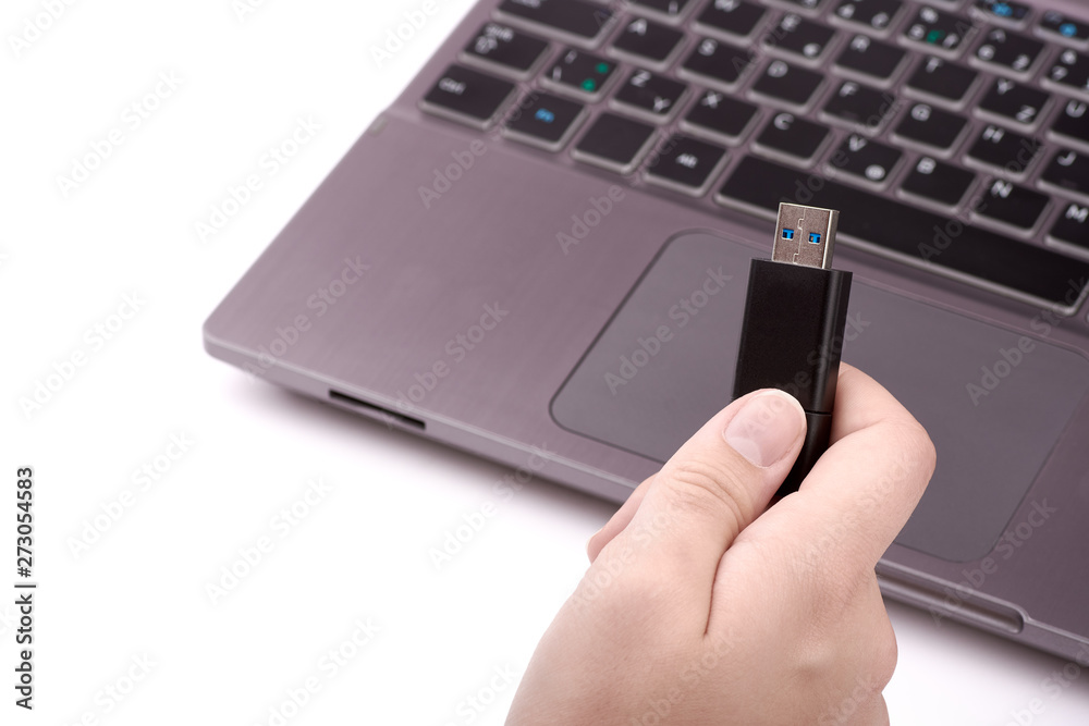Young woman holding a black USB flash drive in her hand, with a defocused silver laptop with a keyboard in the background. Isolated on white. Young woman holding a black USB flash drive in her hand, with a defocused silver laptop with a keyboard in the background. Isolated on white.