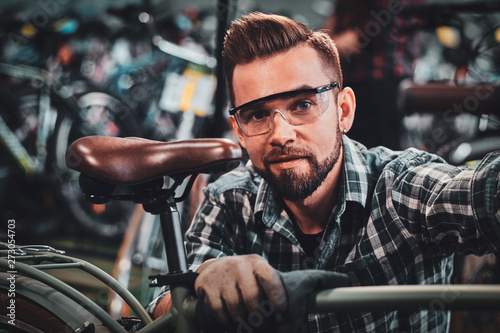 Happy attractive man in protective glasses and shirt is checkin bicycles chain for customer.