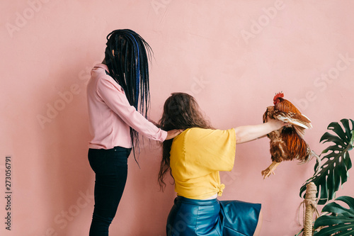 Weird and odd female interracial couple with hair covering their faces. African american girl holding hands on shoulders of her caucasian friend with chicken. photo
