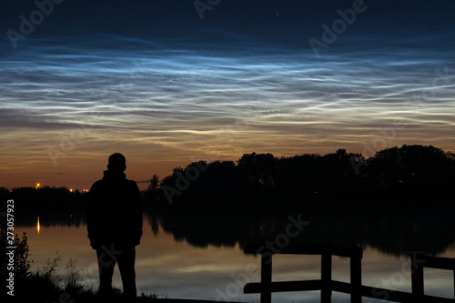 Silhouette of a person looking at noctilucent clouds (NLC, night clouds) near a lake in Holland in the evening. © Menyhert