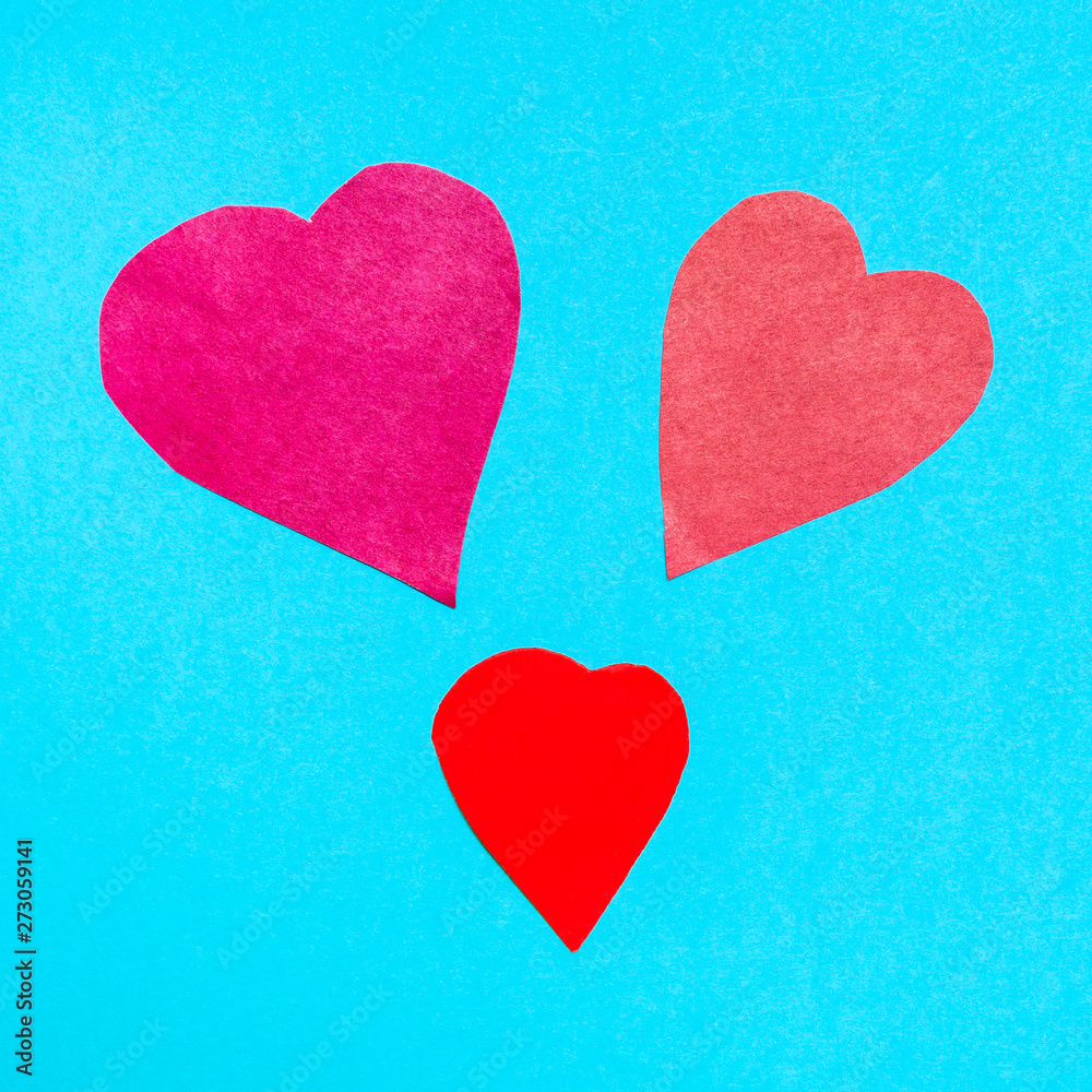 three various hearts cut from red papers on blue