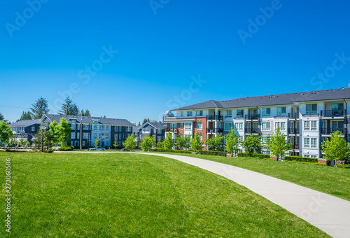 Concrete pathway across huge green lawn in front of residential condo building. Apartment building on sunny day with blue sky.