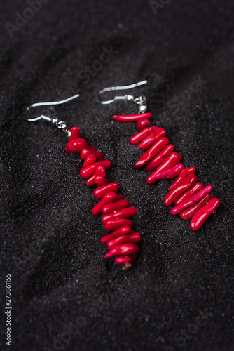 Red coral eardrops on black sand, close up photo