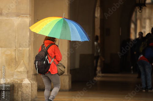 A girl in bright autumn clothes with a large umbrella of all colors of the rainbow walks in the city in the rain. Gay parade of equality. Walk in rainy weather with a trendy gadget. Melancholic