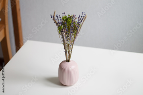 dry lilac and green flowers in pink small vase on white table and light background