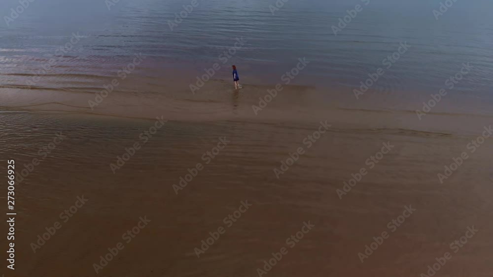 Aerial: Young woman in blue bright dress walking around - Shallow water scenic yellowish sunset landscape at the Baltic Sea - Drone flying view from above Aerial: Young woman in blue bright dress walking around - Shallow water scenic yellowish sunset landscape at the Baltic Sea - Drone flying view from above