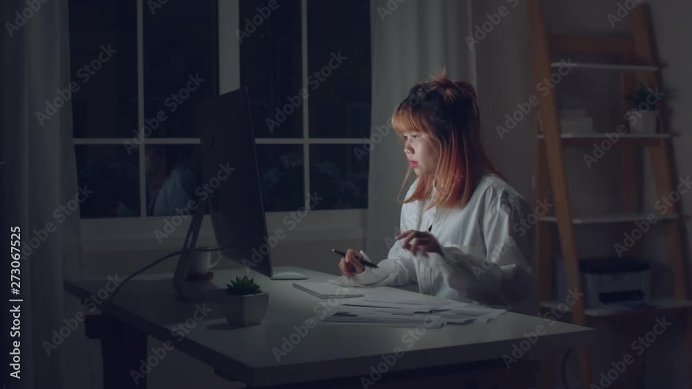 Young asian woman working late using desktop on desk in living room at home. Asia business woman writing notebook document finance and calculator in night at home office. Overworked female concept. Young asian woman working late using desktop on desk in living room at home. Asia business woman writing notebook document finance and calculator in night at home office. Overworked female concept.