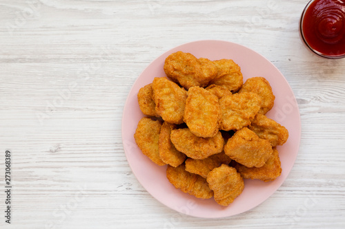 Chicken nuggets on a pink plate, ketchup on a white wooden surface, top view. Overhead, from above, flat lay. Copy space.