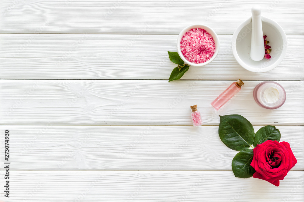 Cream, bath salt, lotion for organic cosmetics with rose flower on white wooden background top view space for text