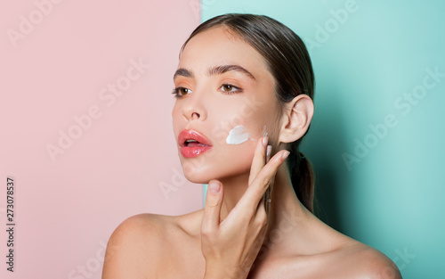 Attractive girl putting anti-aging cream on her face. Closeup Portrait Of Girl With Healthy Smooth Skin. photo