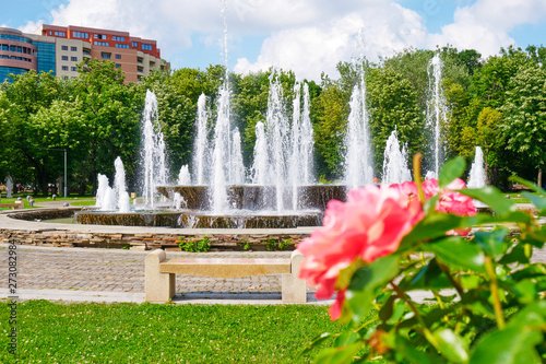 Artesian fountain in a Bucharest city park (Alexandru Ioan Cuza park/IOR) with coral/pink roses and an apartments building in the back, during a very hot Summer day. photo