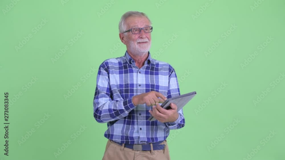 Happy senior bearded hipster man thinking while using digital tablet Happy senior bearded hipster man thinking while using digital tablet