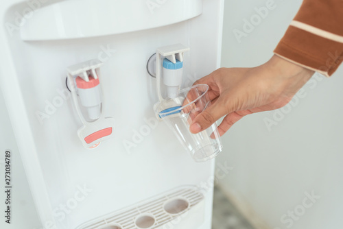 Close up woman filling plastic glass from water cooler machine.