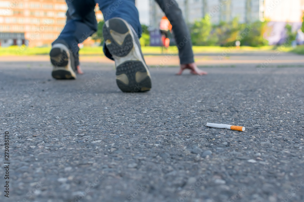 an abandoned Smoking cigarette butt lies on the asphalt path against the background of a man's legs who is preparing to run sprint an abandoned Smoking cigarette butt lies on the asphalt path against the background of a man's legs who is preparing to run sprint