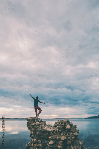 The girl stands on a pile of stones and looks at the sea.