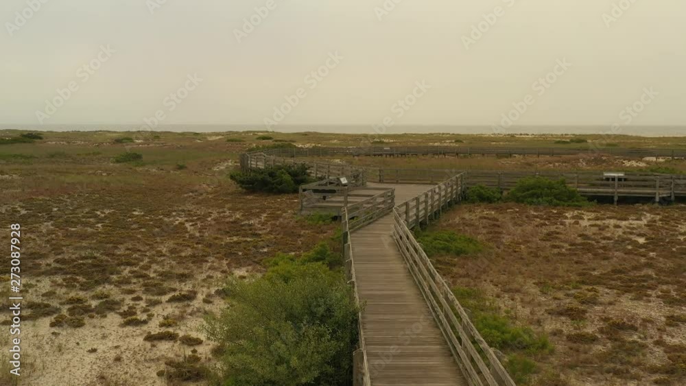 a low, slow drone flight over a wooden walking path flying towards a gray beach and cloudy sky in solitude