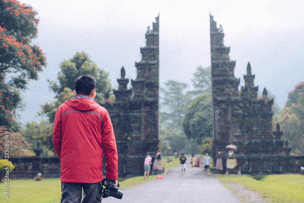 Back view of photographer traveling in Bali and looking to view of traditional Hindu gate in Bali island, Indonesia.