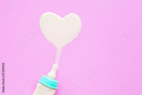 Fototapeta Naklejka Na Ścianę i Meble -  Bottle of milk for baby on pink background. Milk heart shape.