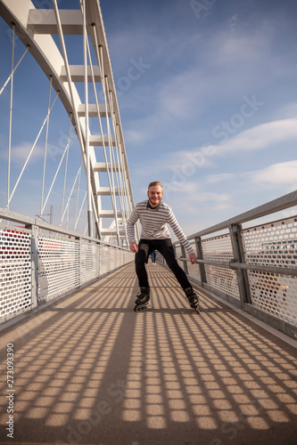 one young man, inline skating on a bridge, looking to camera.