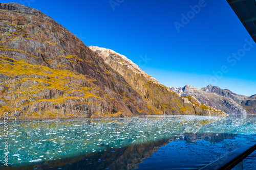 Rocky mountain range in Glacier Bay Alaska with ice/snow covered, broken icebergs floating, reflection in water. Scenic nature tour sailing through the inlet basin in the National Park and Preserve.