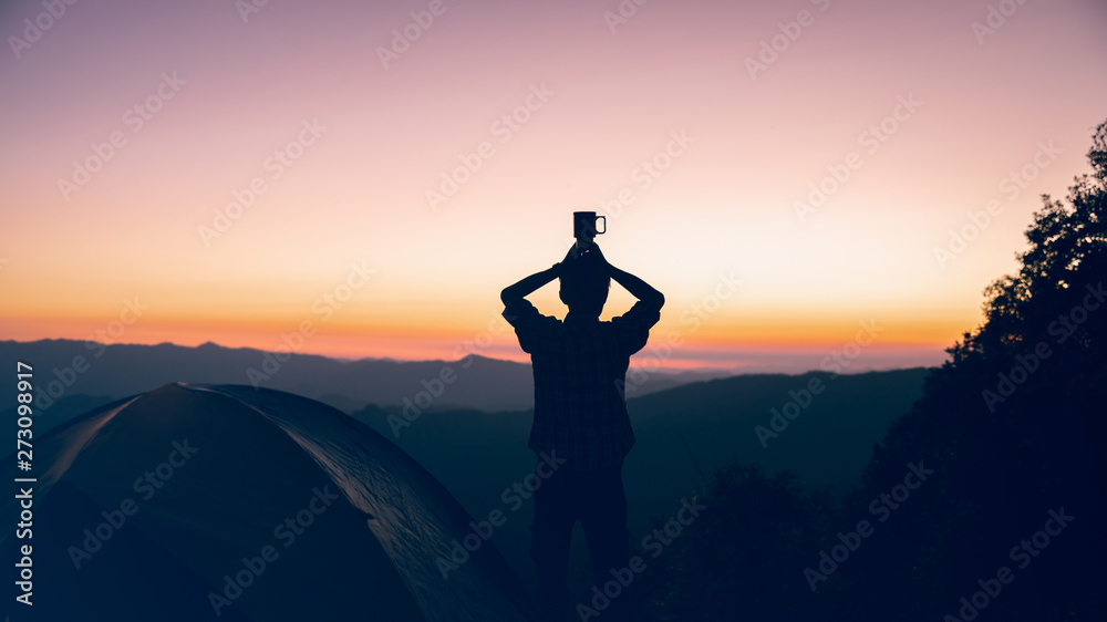 Hiker man holding coffee cup on head near camping tent on mountains at sunset background. travel freedom time concept.