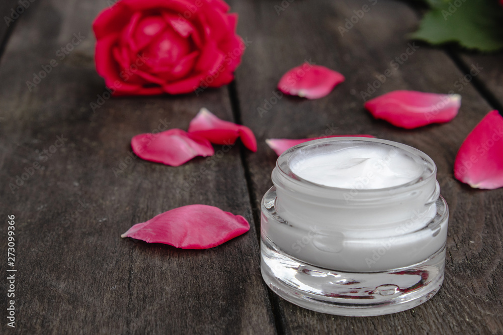 Natural flower cosmetics with red pink flowers for face and body care in a glass jar on a wooden rustic background Natural flower cosmetics with red pink flowers for face and body care in a glass jar on a wooden rustic background