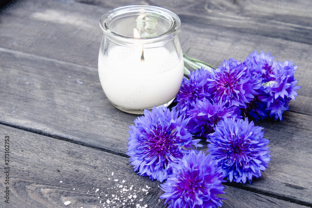 Blue cornflowers and a burning candle on the background of old boards. Blue cornflowers and a burning candle on the background of old boards.