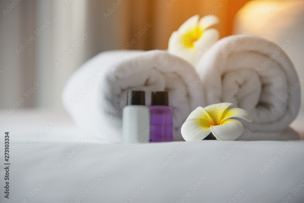 Hotel towel and shampoo and soap bath bottle set on white bed with plumeria flower decorated - relax vacation at the hotel resort concept Hotel towel and shampoo and soap bath bottle set on white bed with plumeria flower decorated - relax vacation at the hotel resort concept