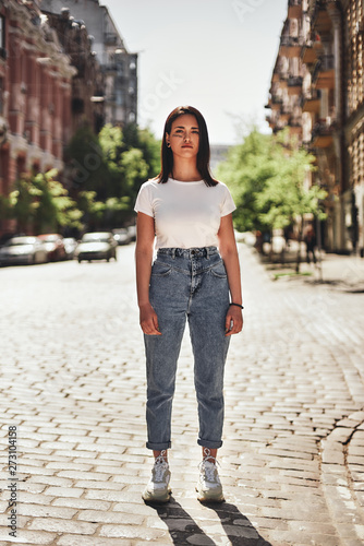 Feeling strong. Vertical photo of young woman in casual clothes standing on the road and looking at camera.