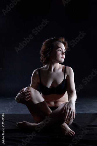 Sexy girl during professional photo shoot in dark room. Model in a black lingerie and erotic underwear