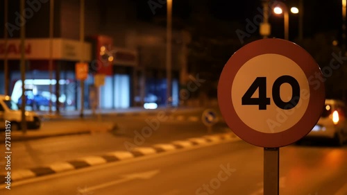 In the city of the Spanish city of Torrevieja at night lit by lanterns. A sign shows a speed limit of 40 in front of a roundabout. Vehicles drive through the circle. Background Bokeh.