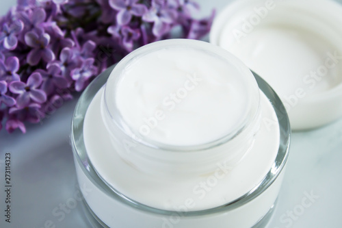 Close up of facial moisturizer cream  on white background. Detail of glass jar of bio moisturizer with flowers. Organic lotion for skincare treatment. Natural beauty and skin care concept.