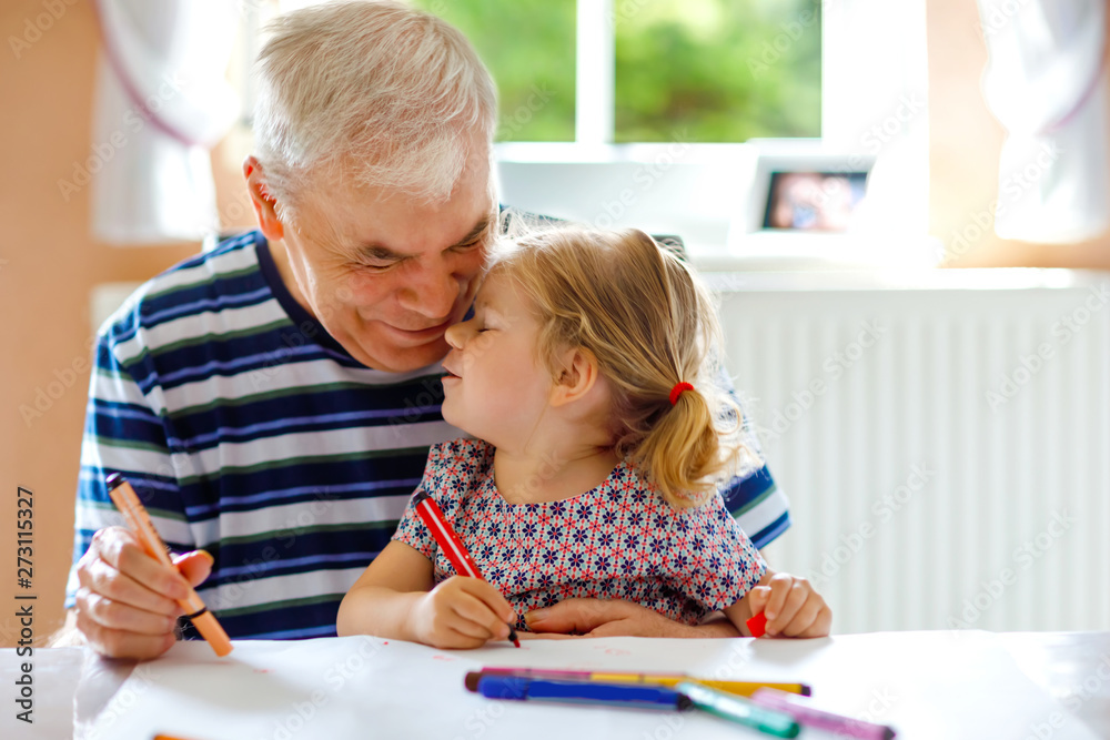 Cute little baby toddler girl and handsome senior grandfather painting with colorful pencils at home. Grandchild and man having fun together Cute little baby toddler girl and handsome senior grandfather painting with colorful pencils at home. Grandchild and man having fun together
