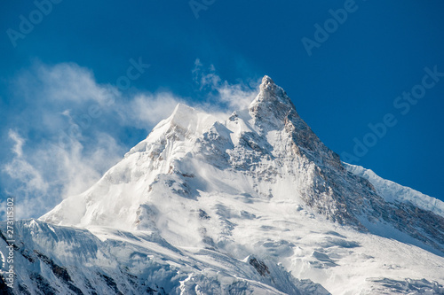 View of snow covered peak of Mount Manaslu (8 156 meters) with clouds in Himalayas, sunny day at Manaslu Glacier in Gorkha District in northern-central Nepal. Detail of snowy peak.