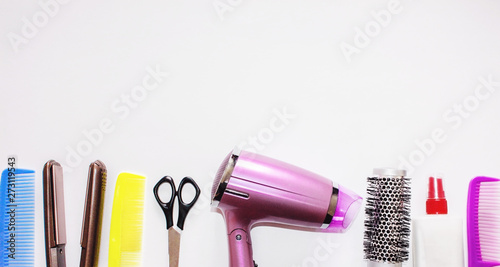 Pink hair dryer, colorful hairbrushes, comb and scissors on white background. Various hair styling devices. Top view. Hair tool set on a white table.
