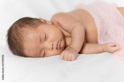 Adorable asian newborn baby in pink wrap sleeping on white blanket background.