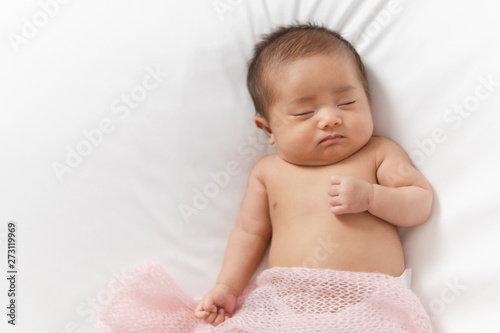 Adorable asian newborn baby in pink wrap sleeping on white blanket background.