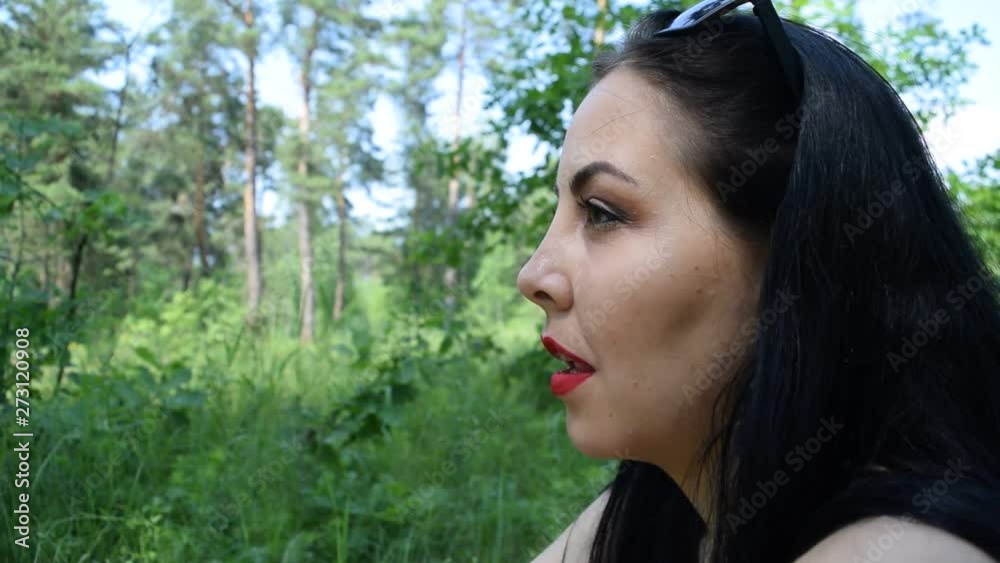 Portrait of a young brunette girl in the forest sitting on the grass.