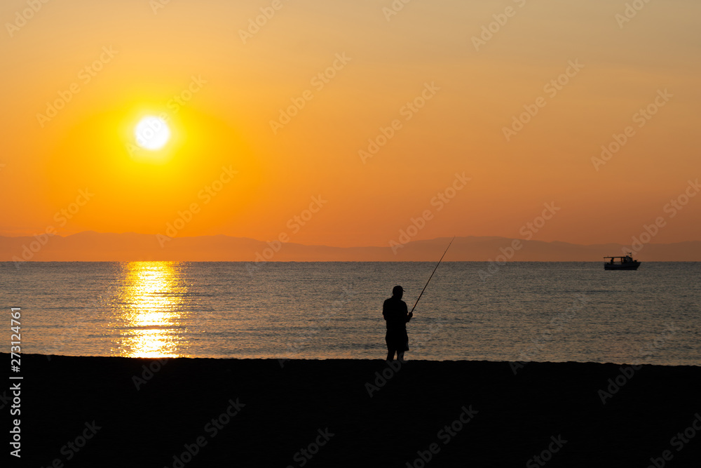Silhouette of a man fishing at the beach in sunrise / sunset  