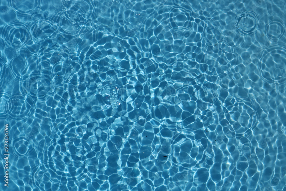 Blue and bright water surface with sun refection in swimming pool for background 