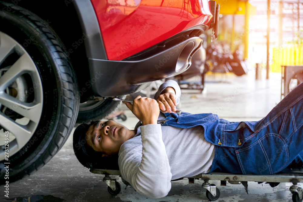 Experienced car mechanic lying down and working under car at auto service garage,repair system of a car. Experienced car mechanic lying down and working under car at auto service garage,repair system of a car.