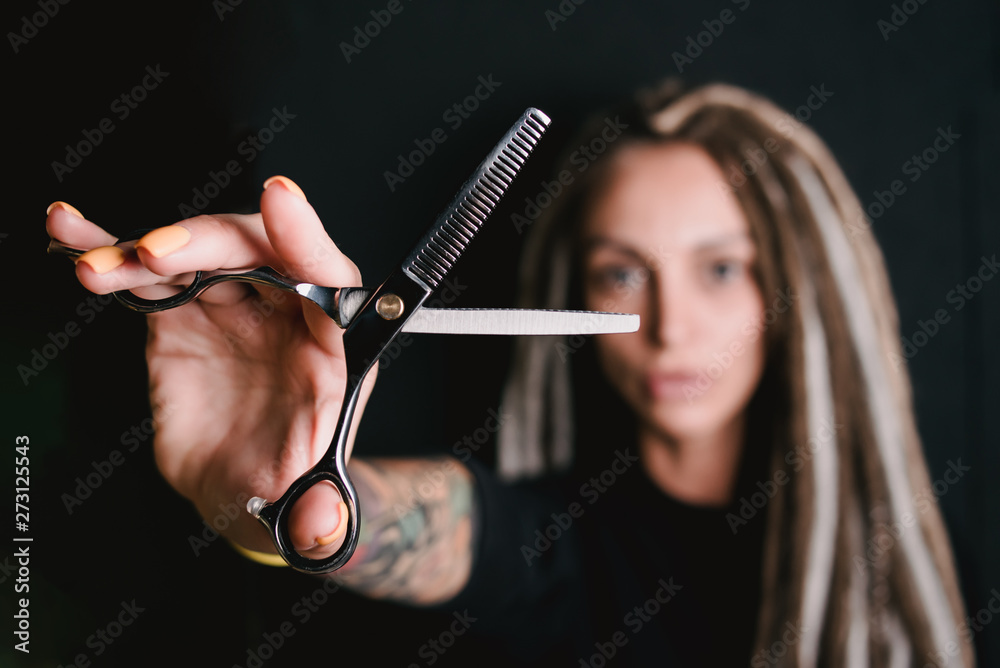 girl hairdresser with dreadlocks holding scissors in hand close-up