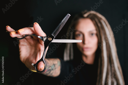 Obraz na płótnie girl hairdresser with dreadlocks holding scissors in hand close-up w salonie