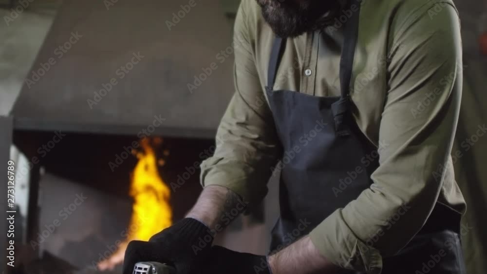 Three shots sequence of Caucasian blacksmith in special uniform holding hand sander with abrasive disk and grinding metal billet lying on anvil Three shots sequence of Caucasian blacksmith in special uniform holding hand sander with abrasive disk and grinding metal billet lying on anvil