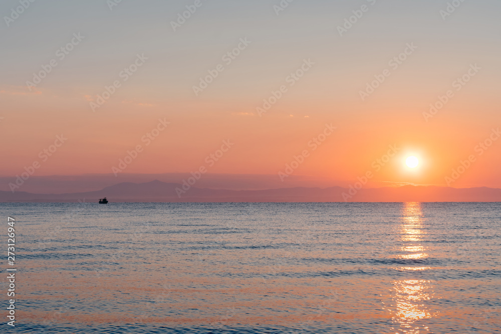 Ship at the sea in bright orange sunset / sunrise with sun in the background