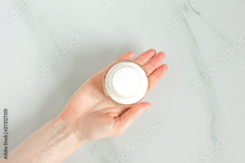 Woman hand with white  hand cream on white background. Cosmetic cream container.Skin care mockup.White jar with open lid of cosmetic cream.